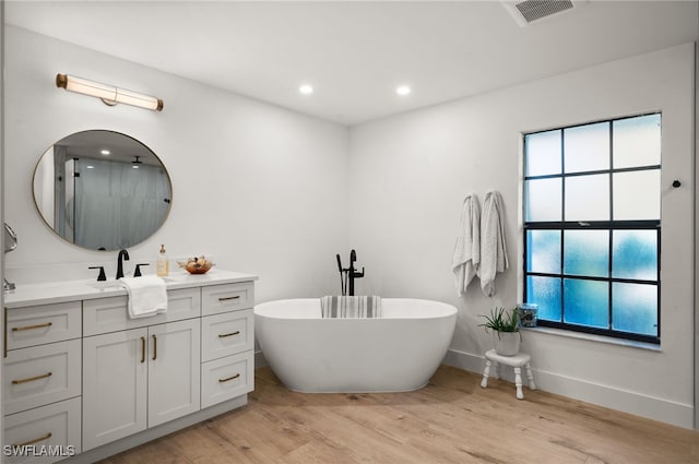 bathroom featuring visible vents, a freestanding bath, recessed lighting, wood finished floors, and vanity