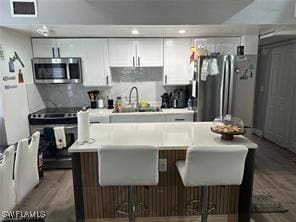 kitchen featuring a breakfast bar area, appliances with stainless steel finishes, wood finished floors, white cabinets, and a sink