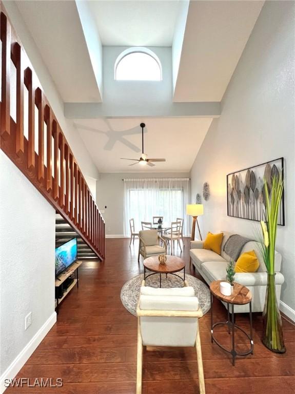 living room featuring stairs, a ceiling fan, baseboards, wood finished floors, and a towering ceiling