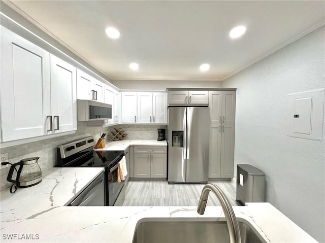 kitchen with electric panel, a sink, tasteful backsplash, appliances with stainless steel finishes, and light stone countertops