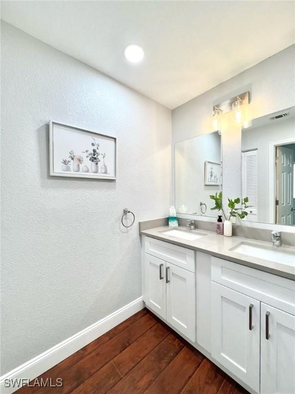 bathroom featuring a sink, baseboards, wood finished floors, and double vanity