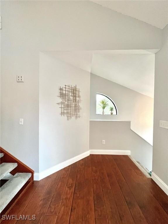 spare room featuring hardwood / wood-style floors, vaulted ceiling, stairway, and baseboards