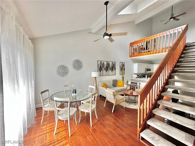 dining area featuring beamed ceiling, wood finished floors, ceiling fan, and stairs