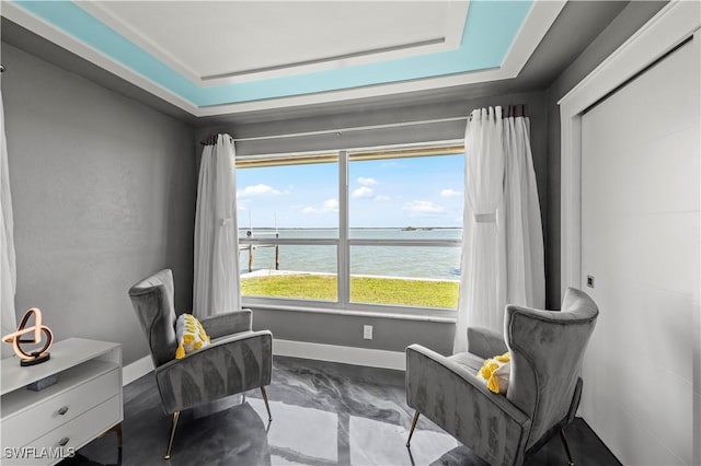 sitting room with a raised ceiling, baseboards, and a water view