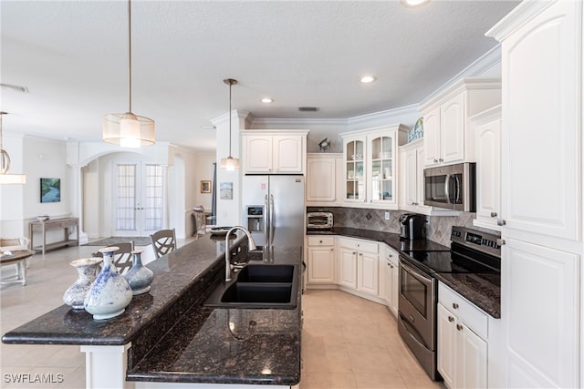 kitchen featuring glass insert cabinets, a center island with sink, decorative backsplash, appliances with stainless steel finishes, and a sink