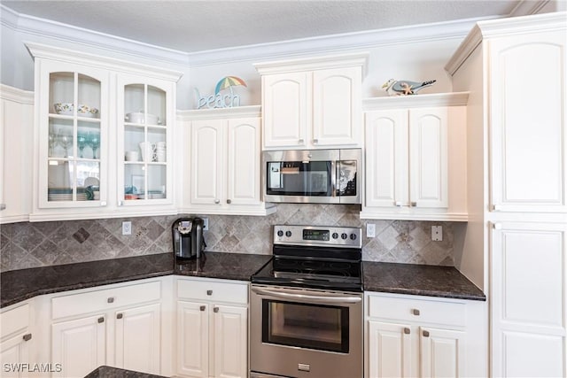 kitchen with white cabinetry, dark stone countertops, glass insert cabinets, and stainless steel appliances