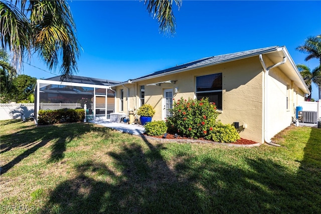 back of house featuring a lanai, fence, a lawn, and stucco siding