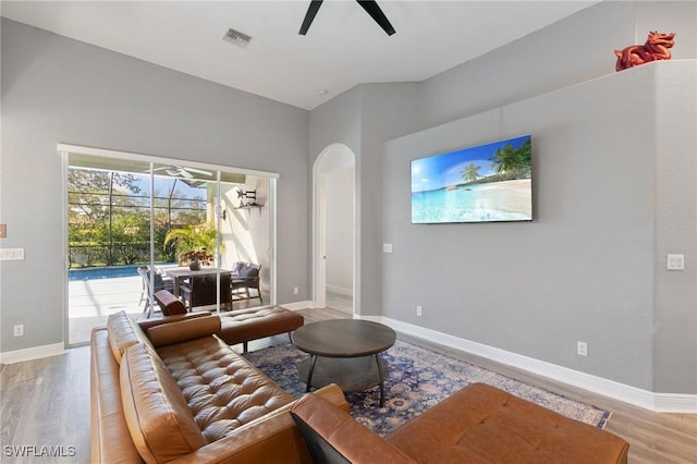 living room featuring baseboards, arched walkways, light wood-style floors, and a ceiling fan