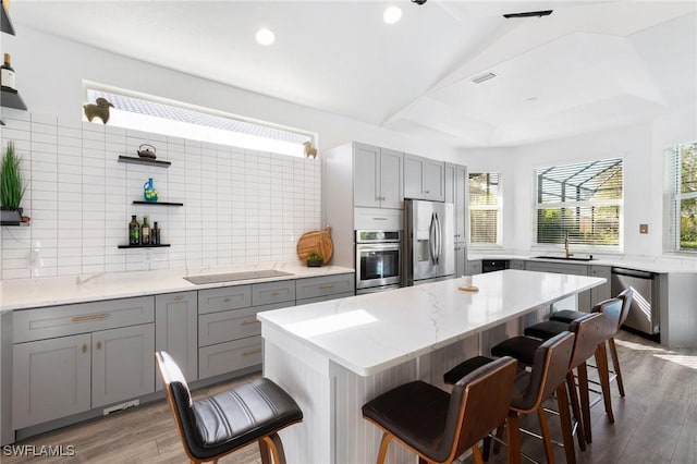 kitchen featuring a breakfast bar area, wood finished floors, open shelves, gray cabinetry, and stainless steel appliances