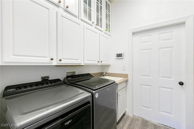 laundry room with washer and clothes dryer, cabinet space, light wood-style flooring, and a sink