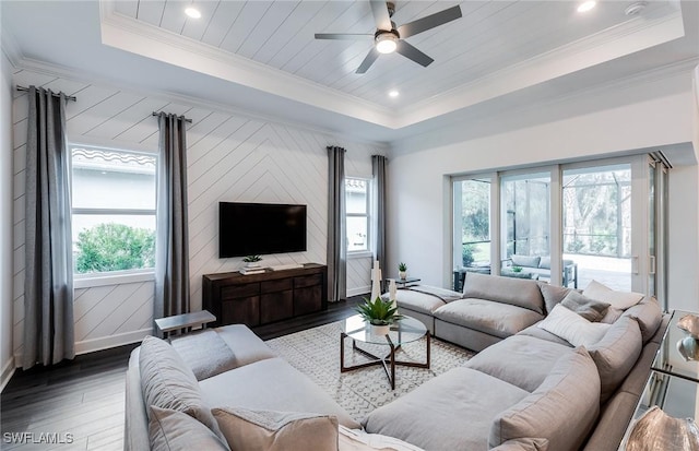 living room with ornamental molding, a raised ceiling, baseboards, and wood finished floors