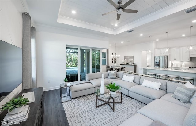 living area featuring visible vents, ornamental molding, ceiling fan with notable chandelier, wood-type flooring, and a raised ceiling