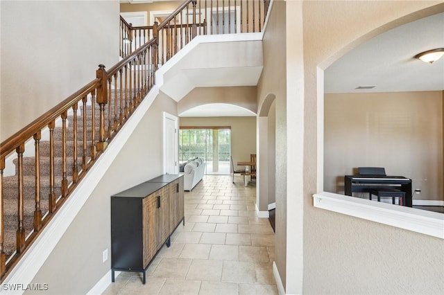foyer entrance featuring light tile patterned flooring, stairs, a high ceiling, baseboards, and arched walkways