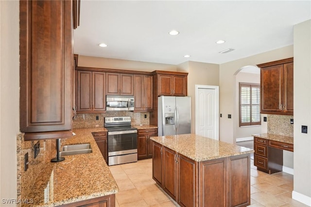 kitchen with visible vents, stainless steel appliances, arched walkways, a sink, and a center island