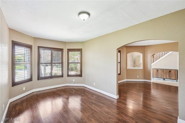 empty room with baseboards, arched walkways, and wood finished floors