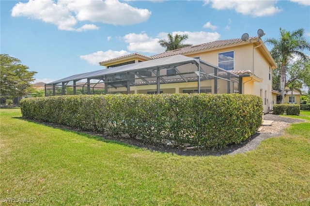 rear view of house with glass enclosure, a lawn, stucco siding, and a tiled roof
