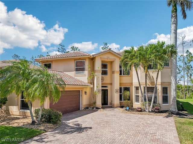 view of front of property featuring stucco siding, an attached garage, a tiled roof, and decorative driveway