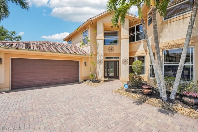 view of front facade featuring stucco siding, an attached garage, a tile roof, and decorative driveway