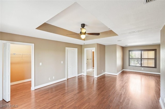 empty room with baseboards, a tray ceiling, wood finished floors, and a ceiling fan