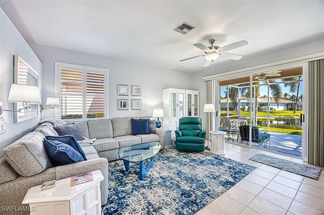 living room featuring tile patterned flooring, visible vents, a ceiling fan, and a water view