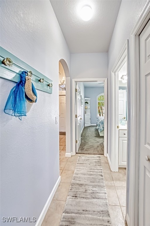 hallway with light tile patterned floors, baseboards, arched walkways, and a textured ceiling