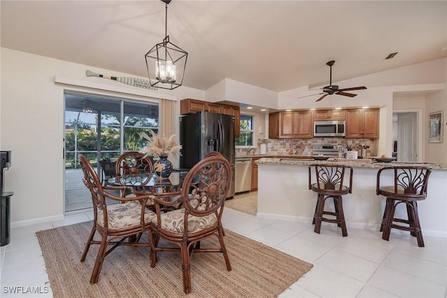 dining space featuring visible vents, baseboards, vaulted ceiling, ceiling fan with notable chandelier, and light tile patterned flooring