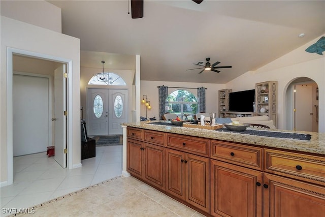 kitchen with ceiling fan, open floor plan, vaulted ceiling, arched walkways, and brown cabinetry