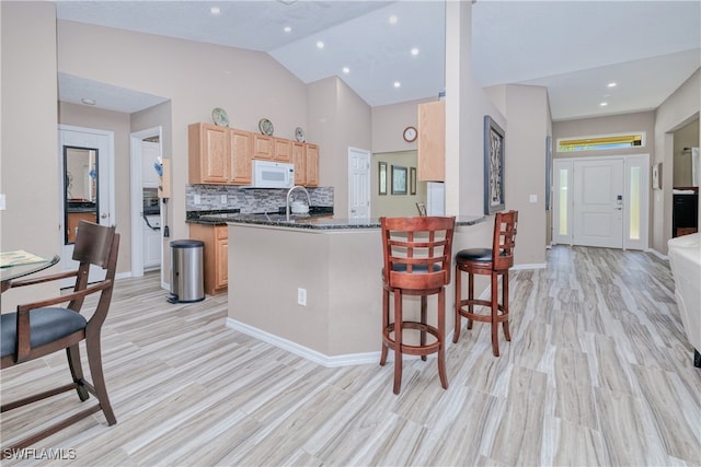 kitchen with a breakfast bar area, white microwave, light brown cabinets, a peninsula, and backsplash