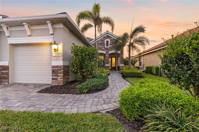 view of front of property featuring stucco siding, stone siding, driveway, and an attached garage