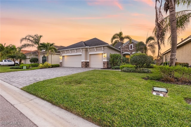 view of front of property featuring a front yard, an attached garage, stucco siding, stone siding, and decorative driveway