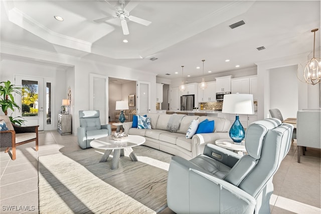 living area featuring visible vents, ceiling fan with notable chandelier, a tray ceiling, light tile patterned flooring, and crown molding