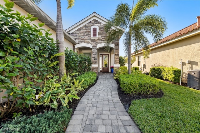 doorway to property with stucco siding, stone siding, and central AC