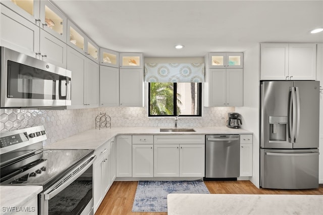 kitchen with tasteful backsplash, light wood-type flooring, appliances with stainless steel finishes, white cabinets, and a sink