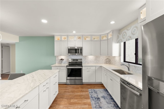 kitchen with light wood-type flooring, decorative backsplash, stainless steel appliances, white cabinetry, and a sink