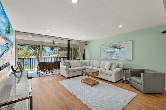 living area featuring a water view, a ceiling fan, wood finished floors, recessed lighting, and a wall of windows