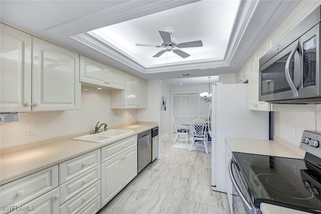 kitchen with a tray ceiling, a sink, light countertops, appliances with stainless steel finishes, and ceiling fan with notable chandelier