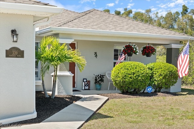 view of exterior entry featuring stucco siding, a lawn, and a shingled roof