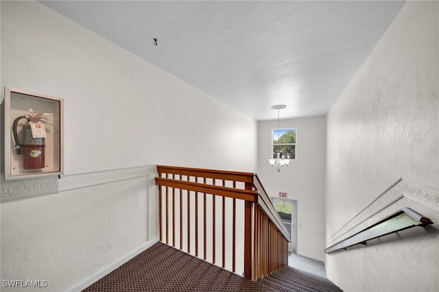 stairs featuring an inviting chandelier, carpet flooring, and a textured wall