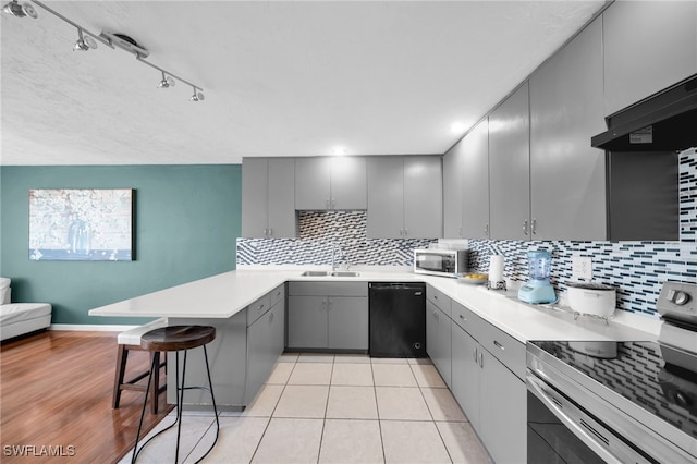 kitchen featuring a breakfast bar, a peninsula, gray cabinets, a sink, and stainless steel appliances