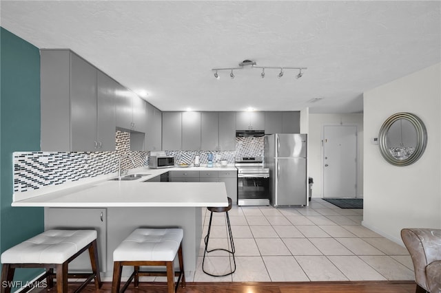 kitchen with a breakfast bar, gray cabinets, a sink, stainless steel appliances, and a peninsula