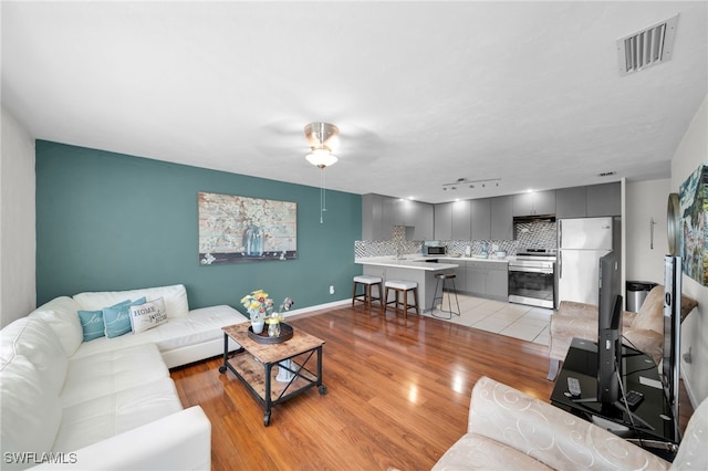 living room featuring baseboards, light wood-style floors, visible vents, and ceiling fan