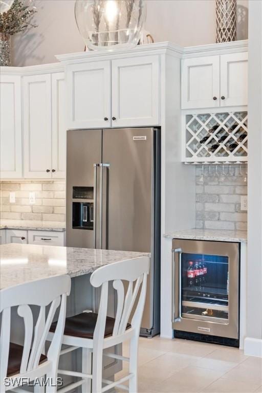 kitchen with light stone counters, stainless steel fridge, beverage cooler, and white cabinets