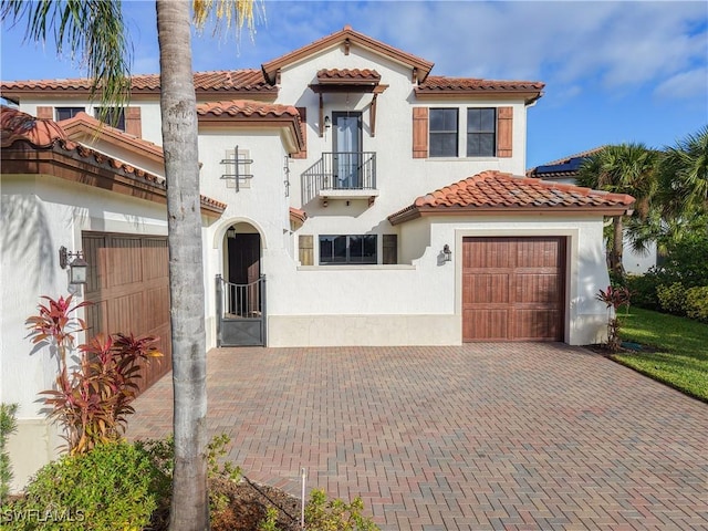 mediterranean / spanish-style home with a tiled roof, stucco siding, decorative driveway, a balcony, and a garage