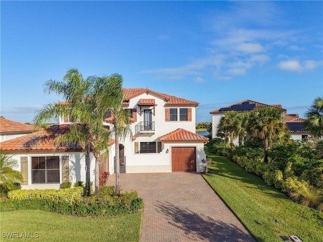 mediterranean / spanish house featuring a tiled roof, stucco siding, decorative driveway, a garage, and a balcony