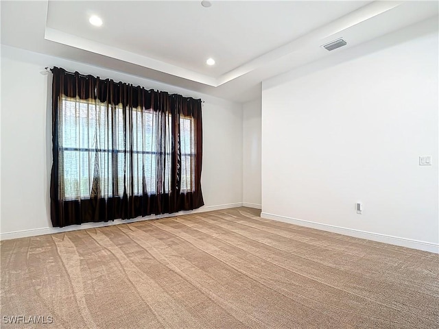 empty room featuring recessed lighting, baseboards, a raised ceiling, and light colored carpet