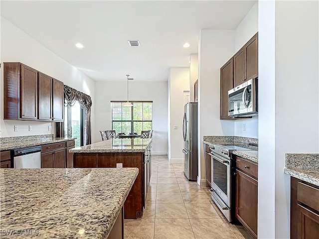 kitchen with light stone countertops, a kitchen island, light tile patterned flooring, stainless steel appliances, and dark brown cabinets