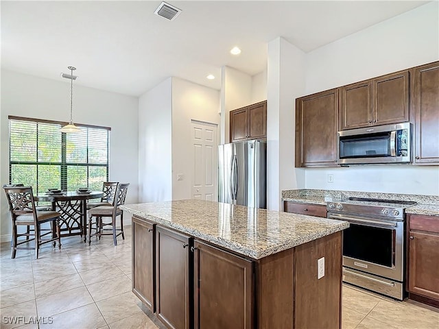 kitchen with visible vents, a center island, stainless steel appliances, light tile patterned floors, and light stone countertops