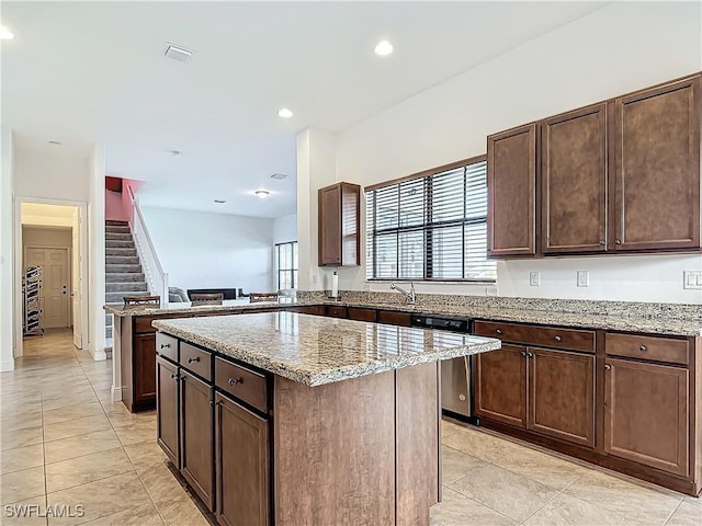 kitchen with light stone counters, a kitchen island, recessed lighting, dark brown cabinets, and stainless steel dishwasher