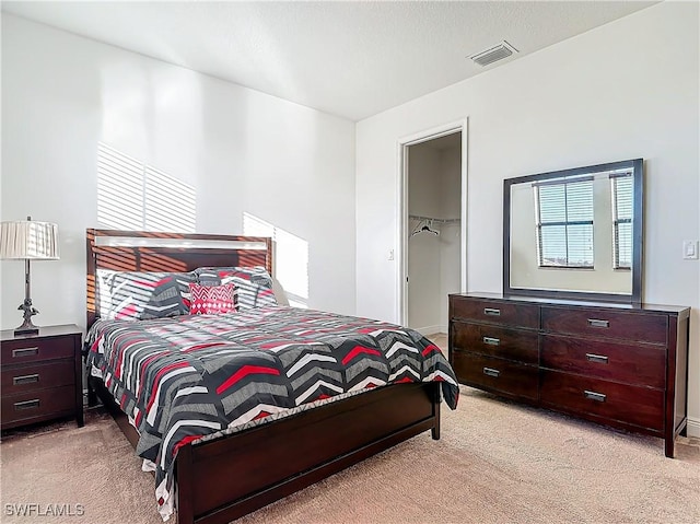 bedroom with a closet, visible vents, light colored carpet, and a walk in closet