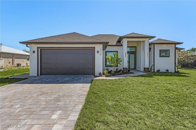 prairie-style house with stucco siding, an attached garage, decorative driveway, and a front yard